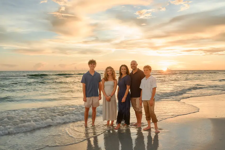 A family of five standing at the edge of the water on Siesta Key, the sun touching the Gulf horizon behind them