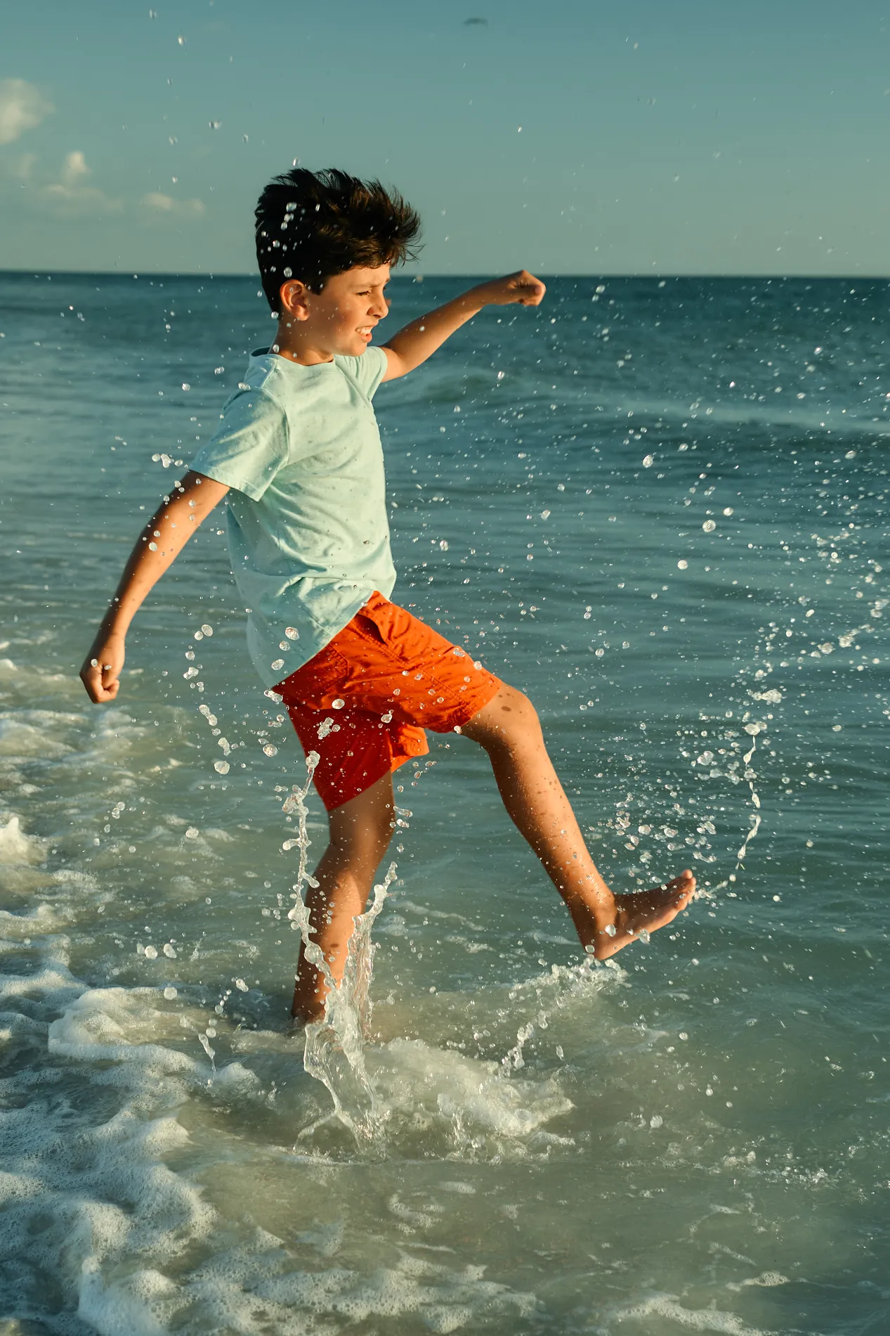 A boy in red shorts kicking up a spray of water on Anna Maria Island