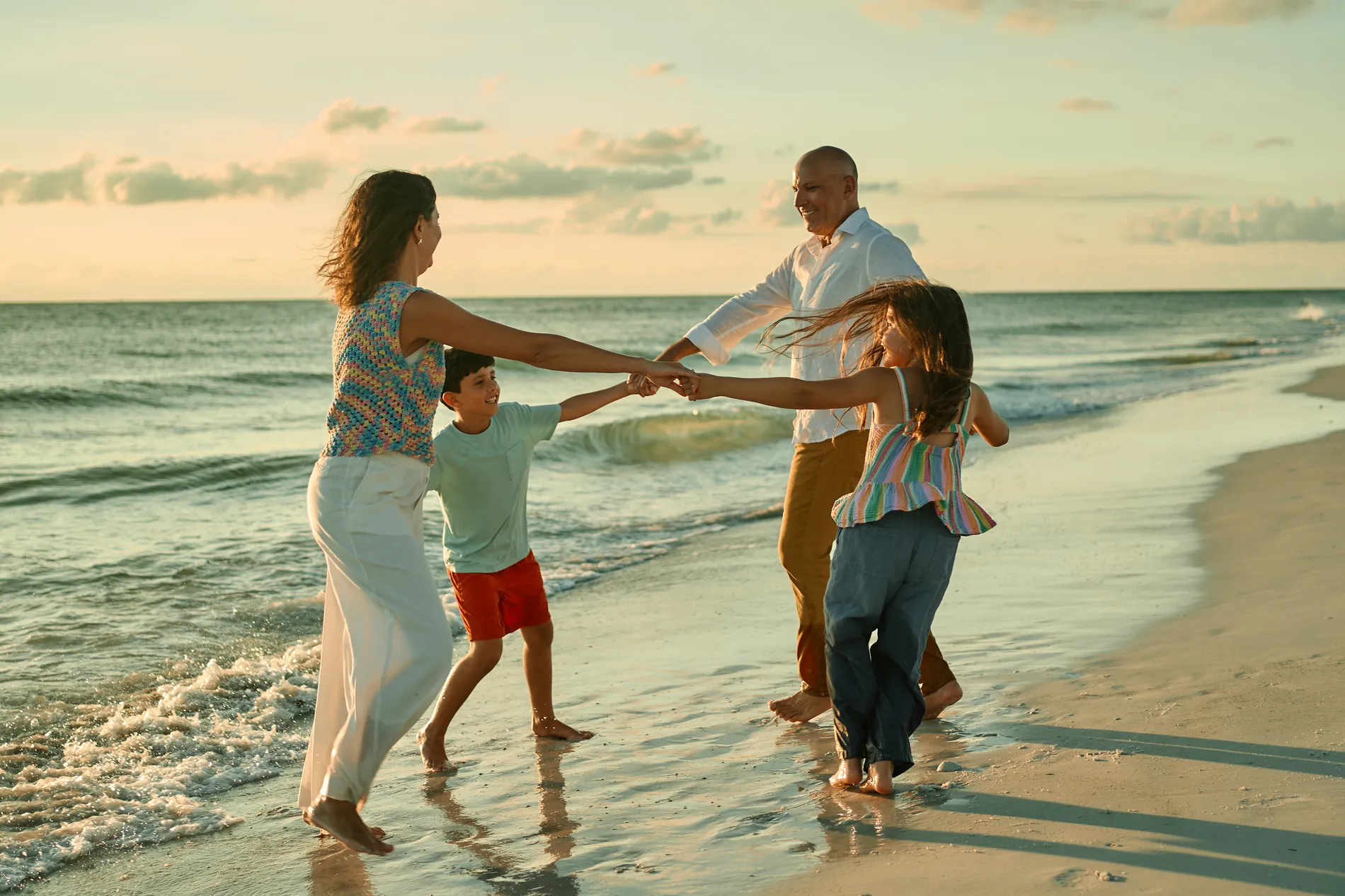 A family holding hands and spinning in a circle in the surf on Anna Maria Island in warm evening light