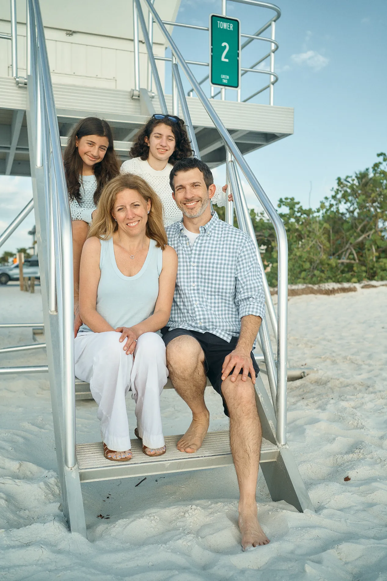 A family of four sitting on the steps of a white lifeguard stand on Anna Maria Island, the two teenage daughters behind their parents