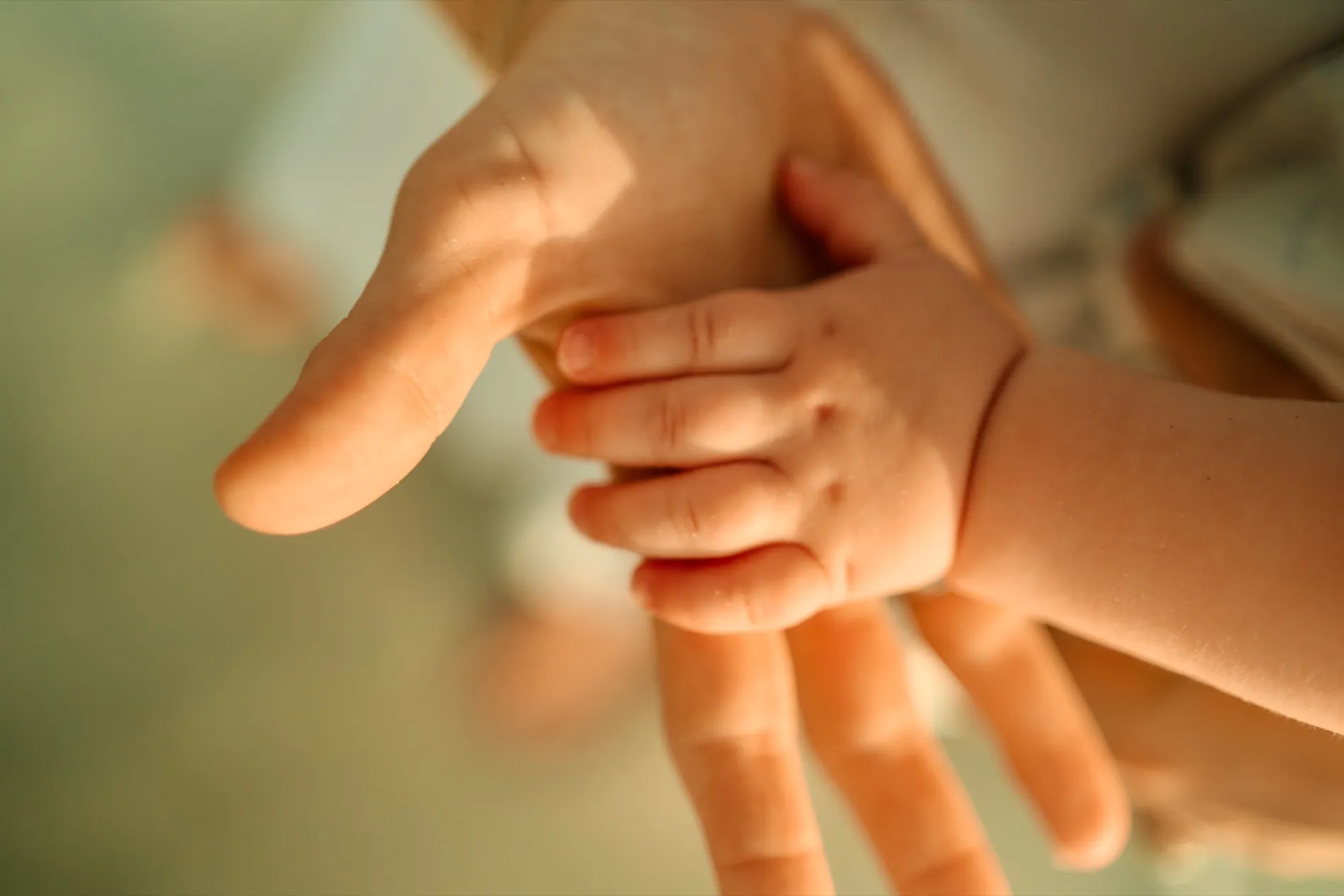 A baby's hand gripping a parent's finger