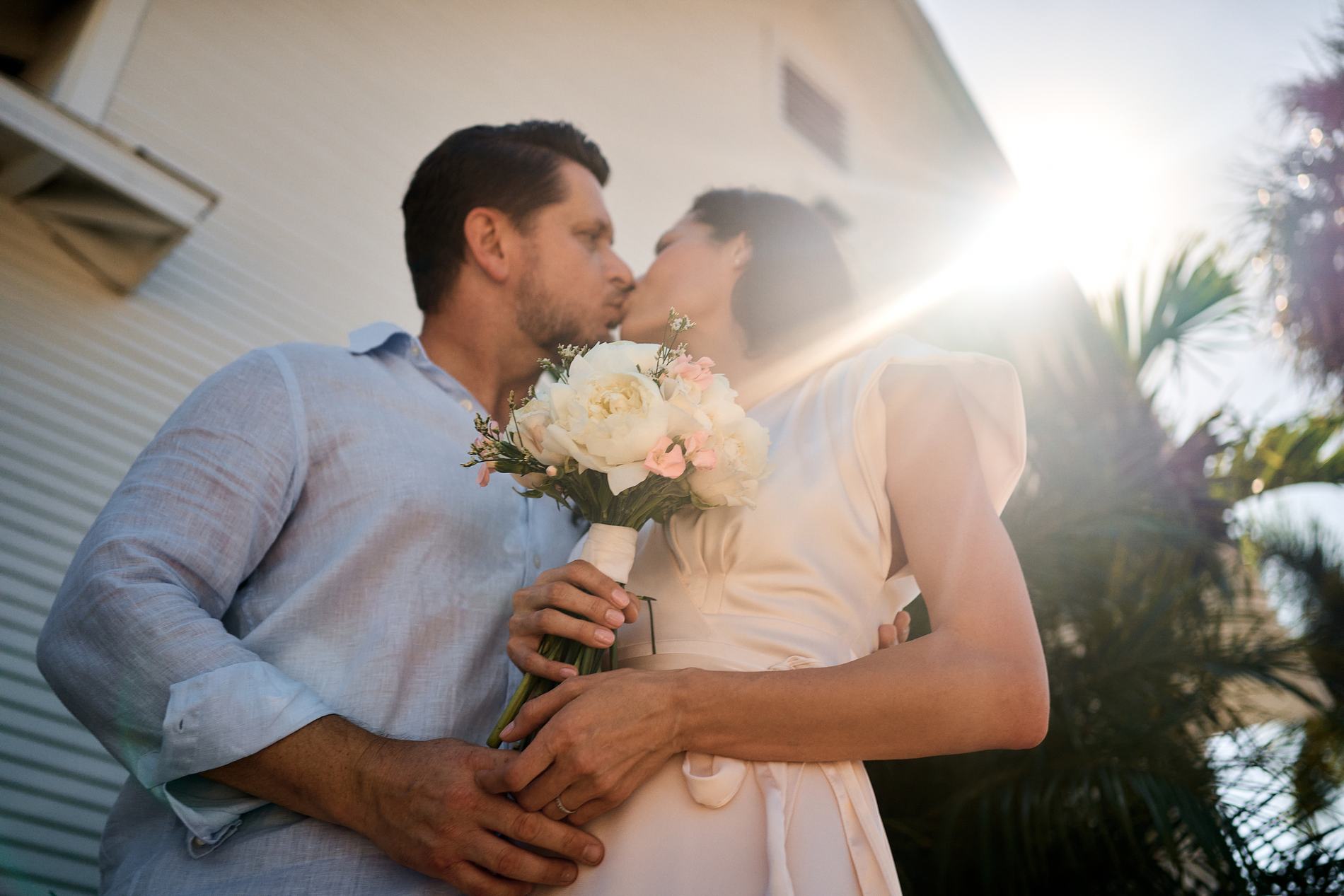 A bride and groom kissing in the sun next to a white chapel on Boca Grande