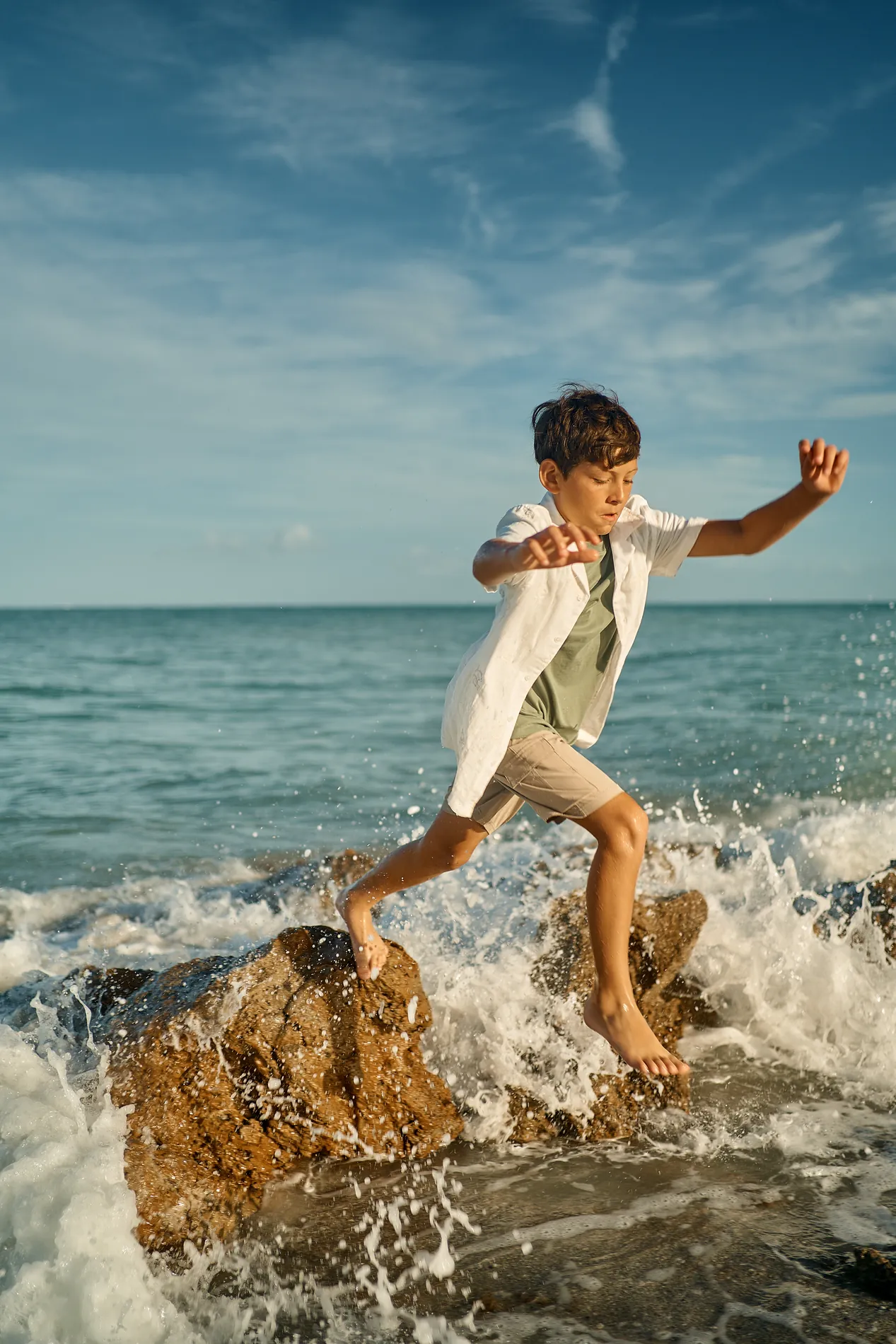 A boy jumping off a dark rock into the surf at Caspersen Beach in Venice