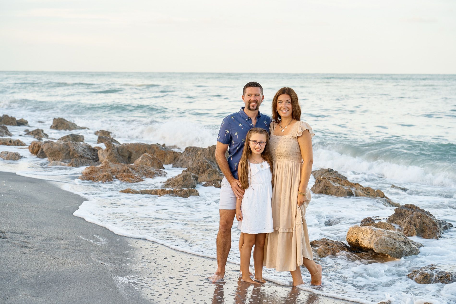 A family standing among the rocks at the water on Caspersen Beach in Venice, waves breaking behind them