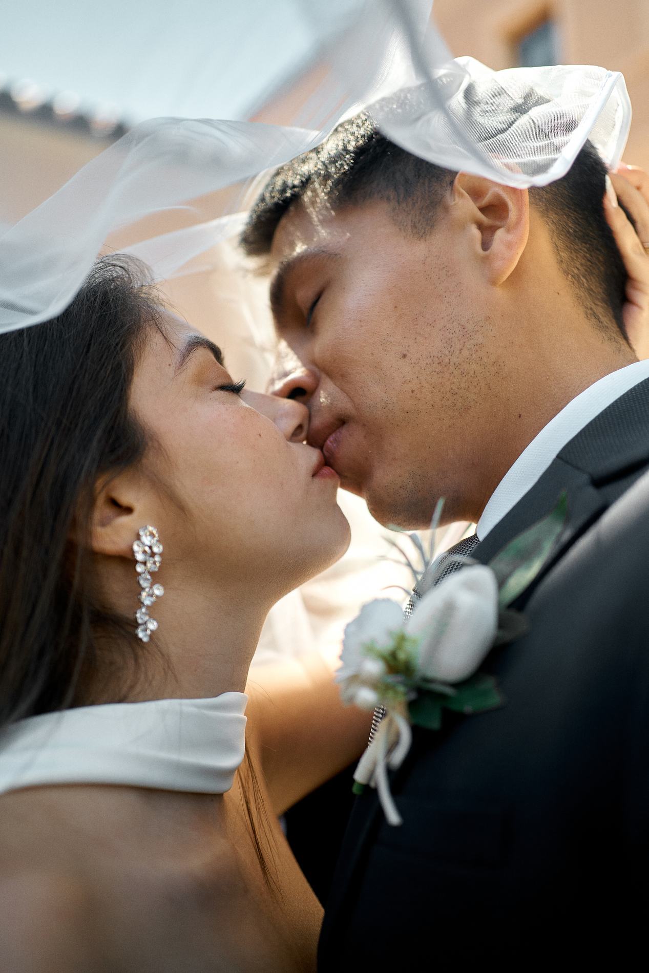 A bride and groom kissing, her veil lifted by the wind