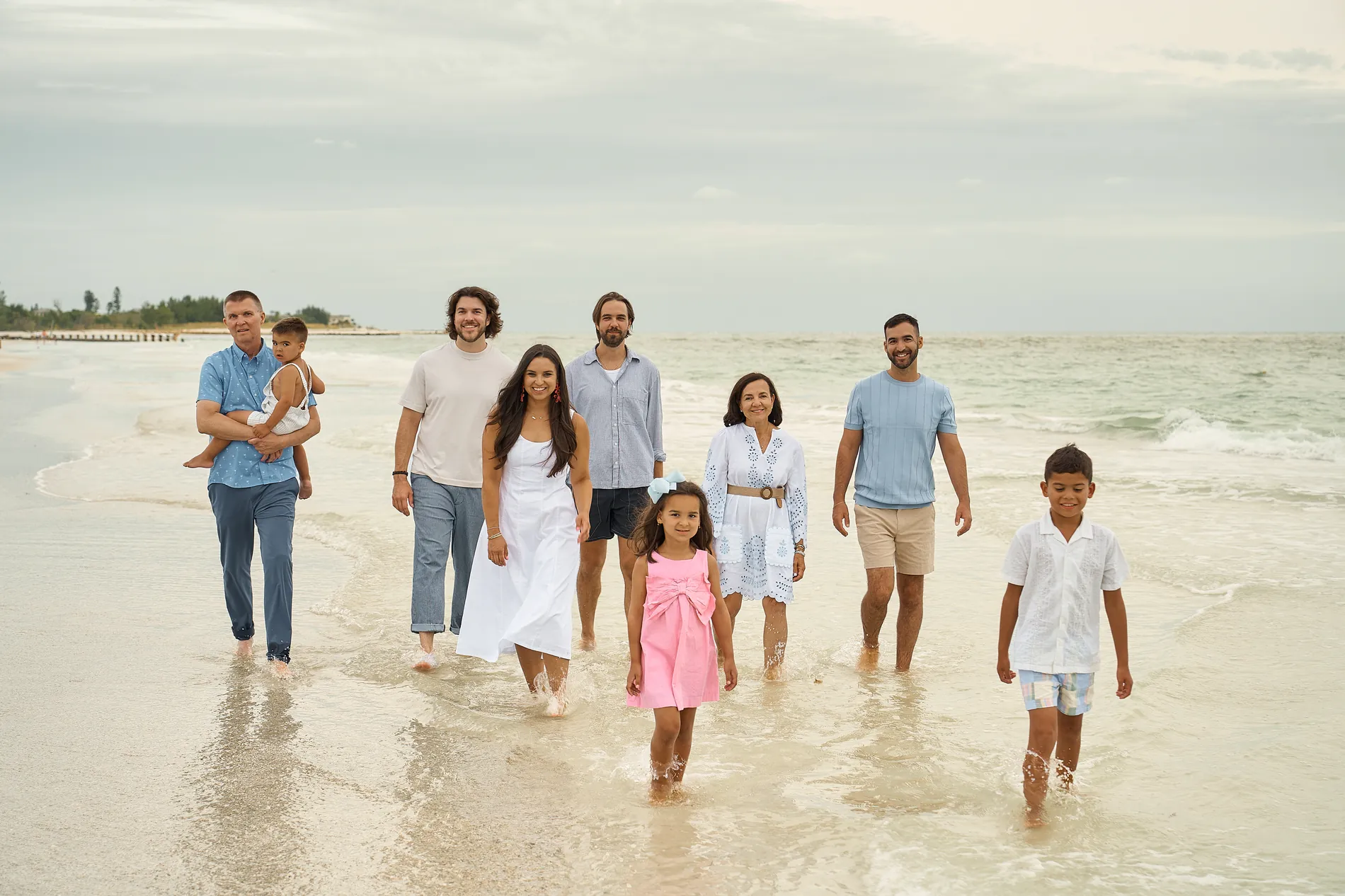 Nine people of one family walking toward the camera through the shallow water at Coquina Beach