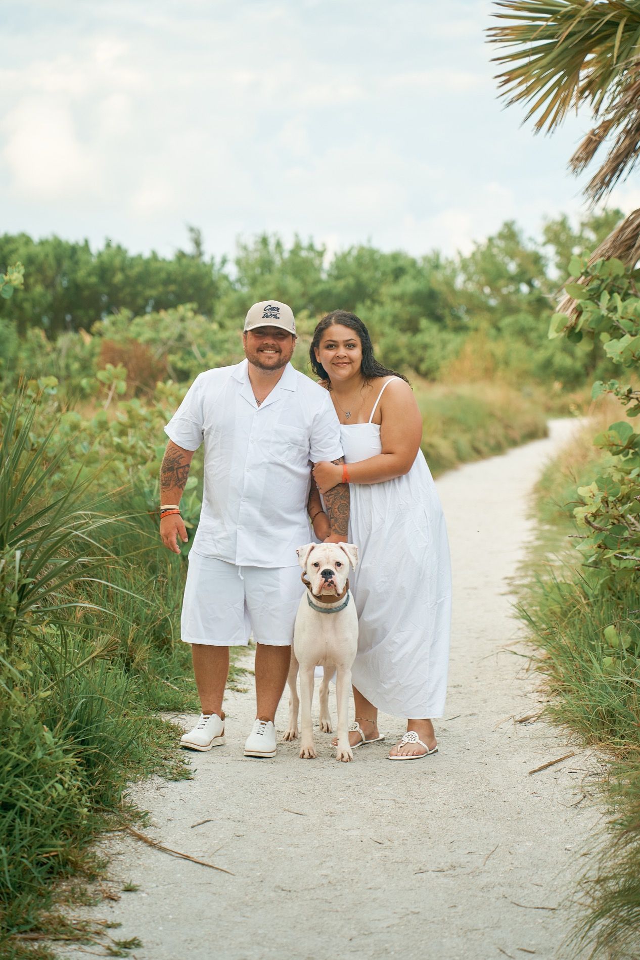 A couple in white walking their dog down a sandy path