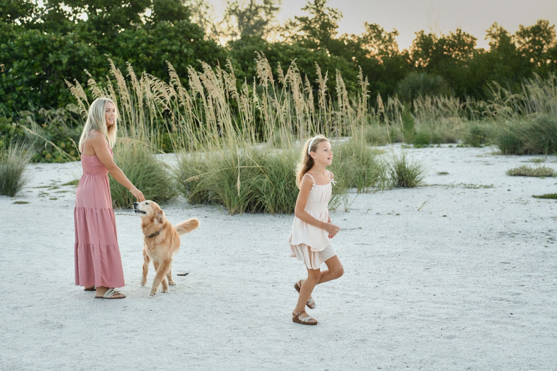A mother and daughter walking with their golden retriever through the dune grass