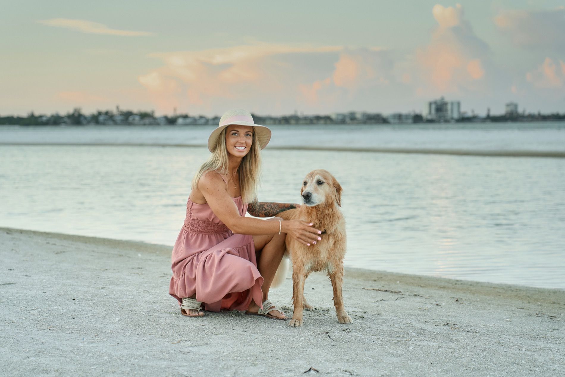 A woman crouching beside her dog at the water's edge