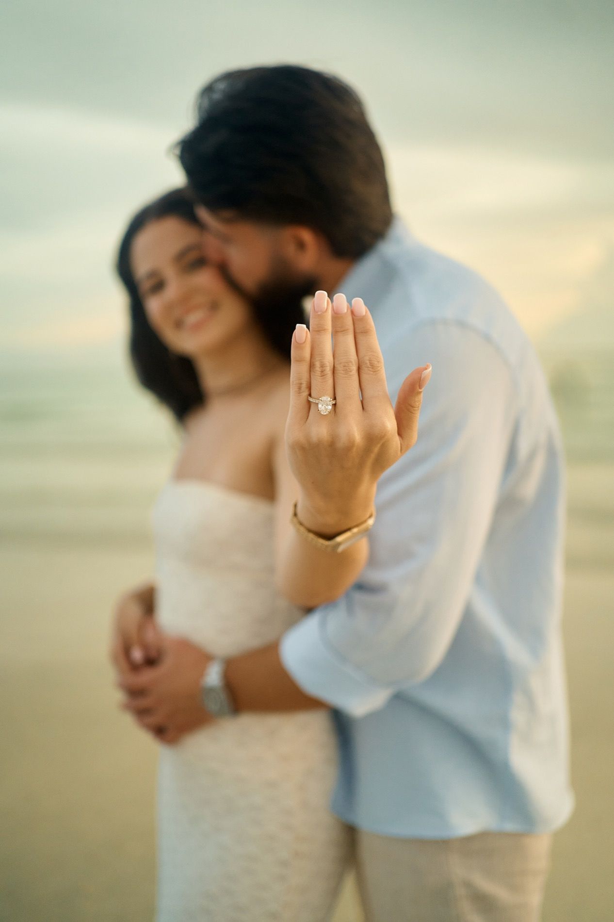 A newly engaged woman showing her ring while her partner holds her on the beach