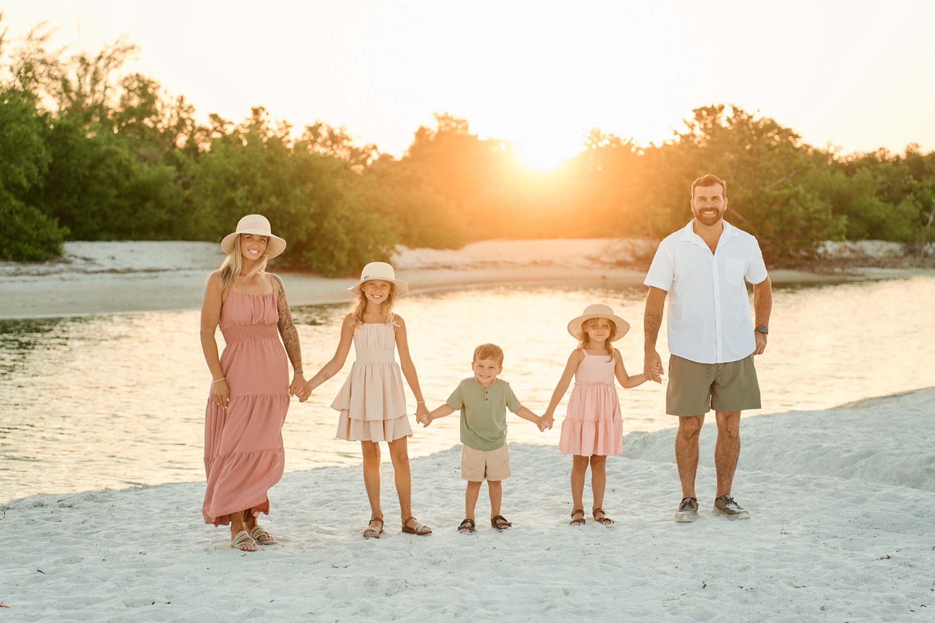 A family of five holding hands in a row on the beach at sunset