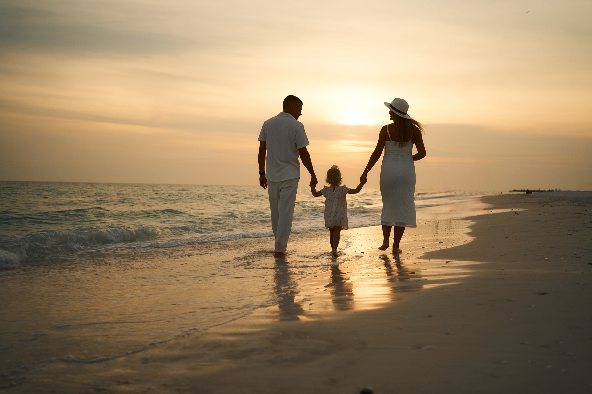 A family of three in silhouette walking hand in hand into the sunset on Lido Key