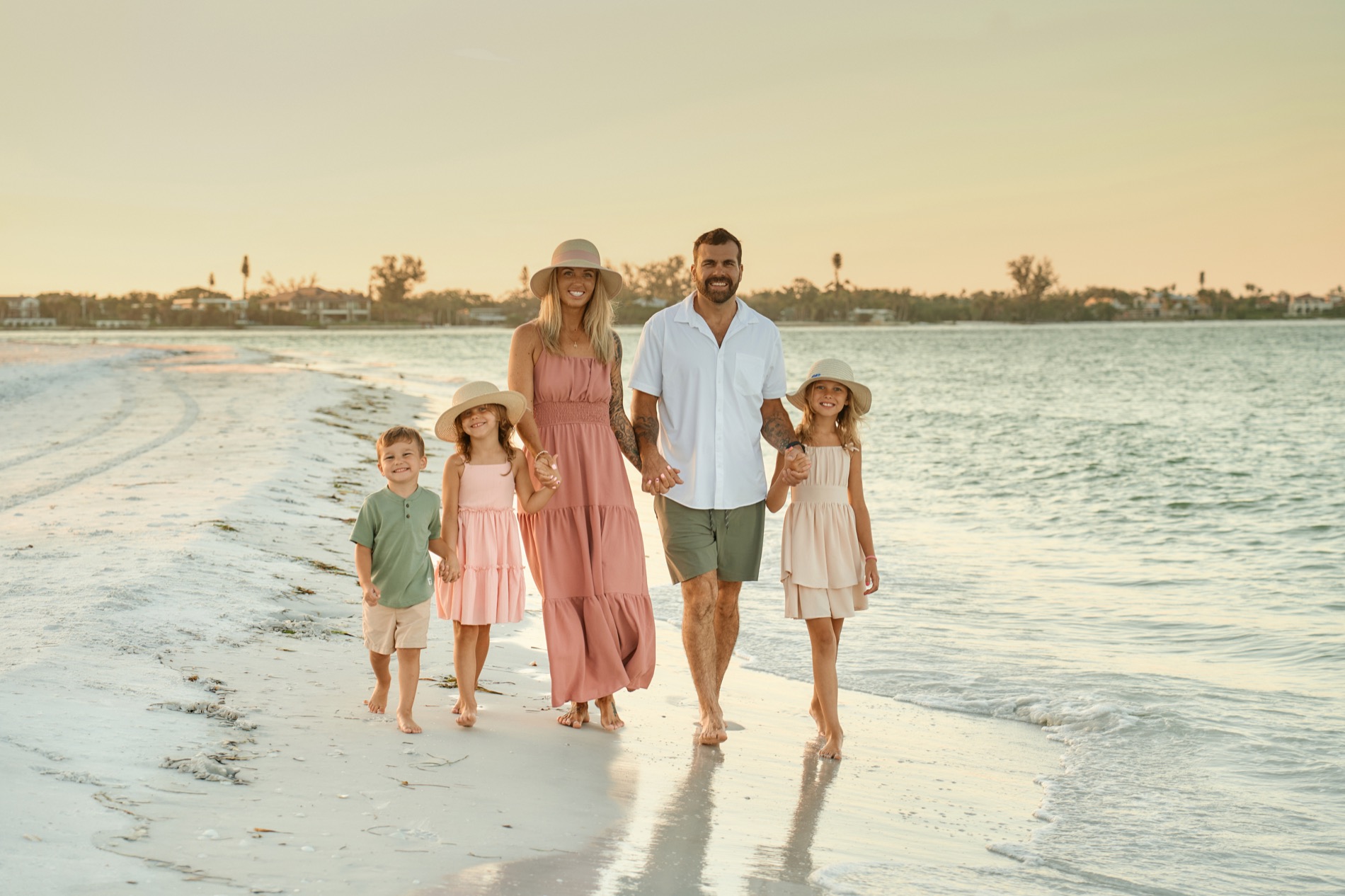 A family of five walking hand in hand along the shoreline at sunset on a Sarasota beach