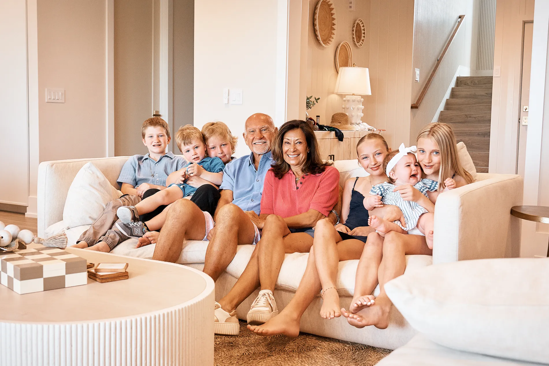 Grandparents on a white sofa in their vacation home on Anna Maria Island with six grandchildren around them, from a baby in a bow to a boy of about ten, everyone laughing