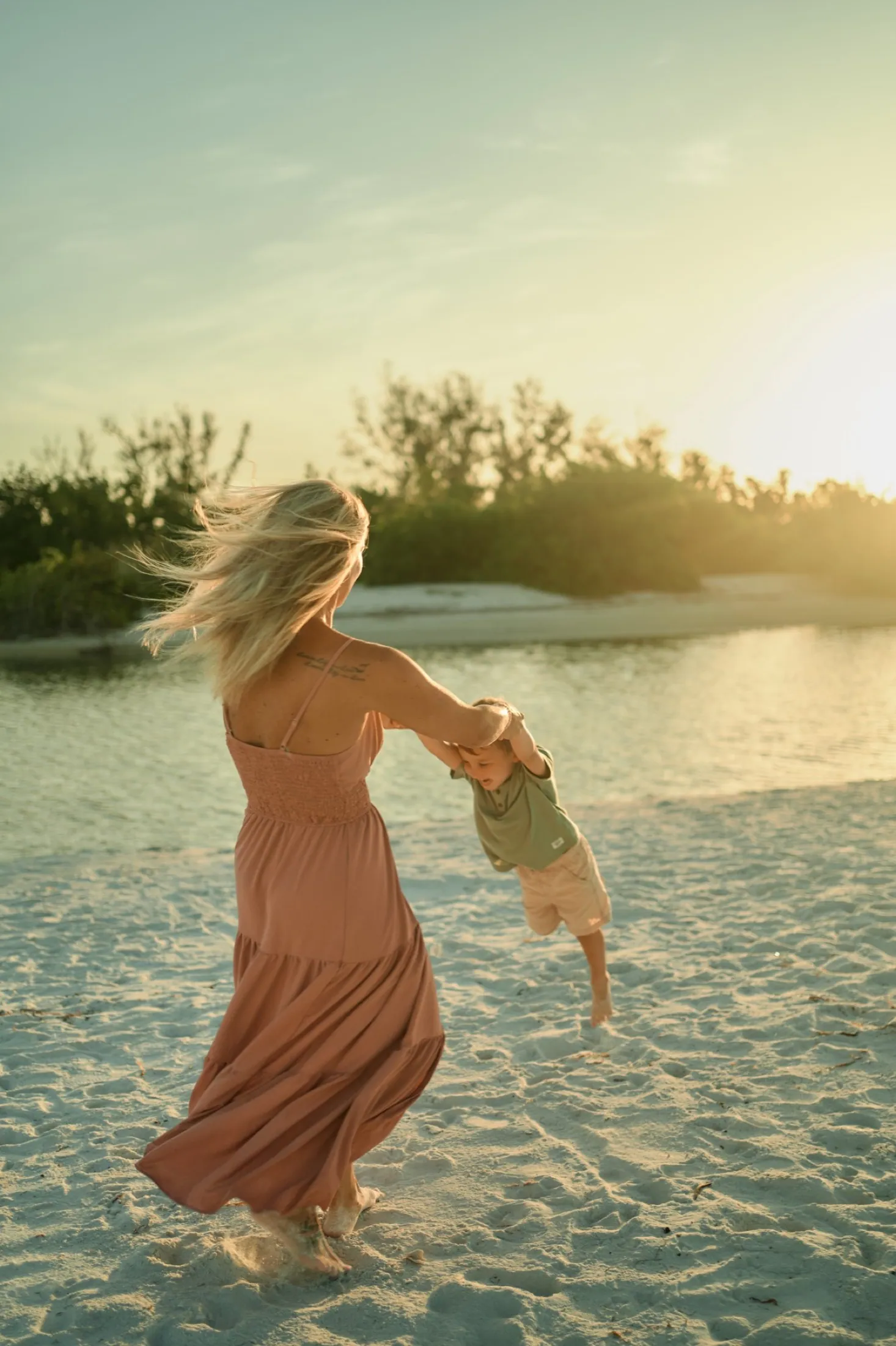 A mother swinging her son on the sand at sunset