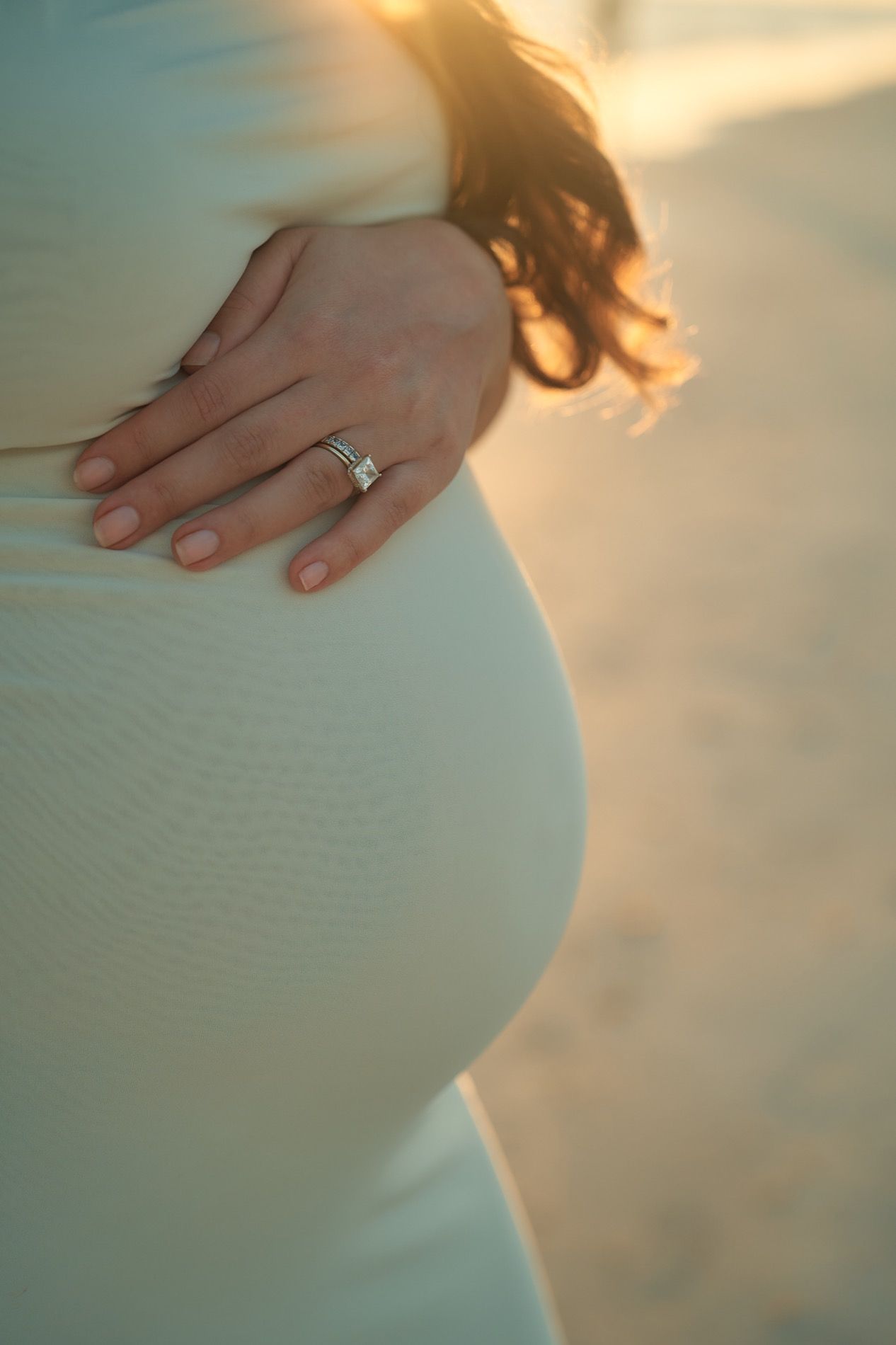 A close photograph of hands resting on the belly, a ring catching the evening light