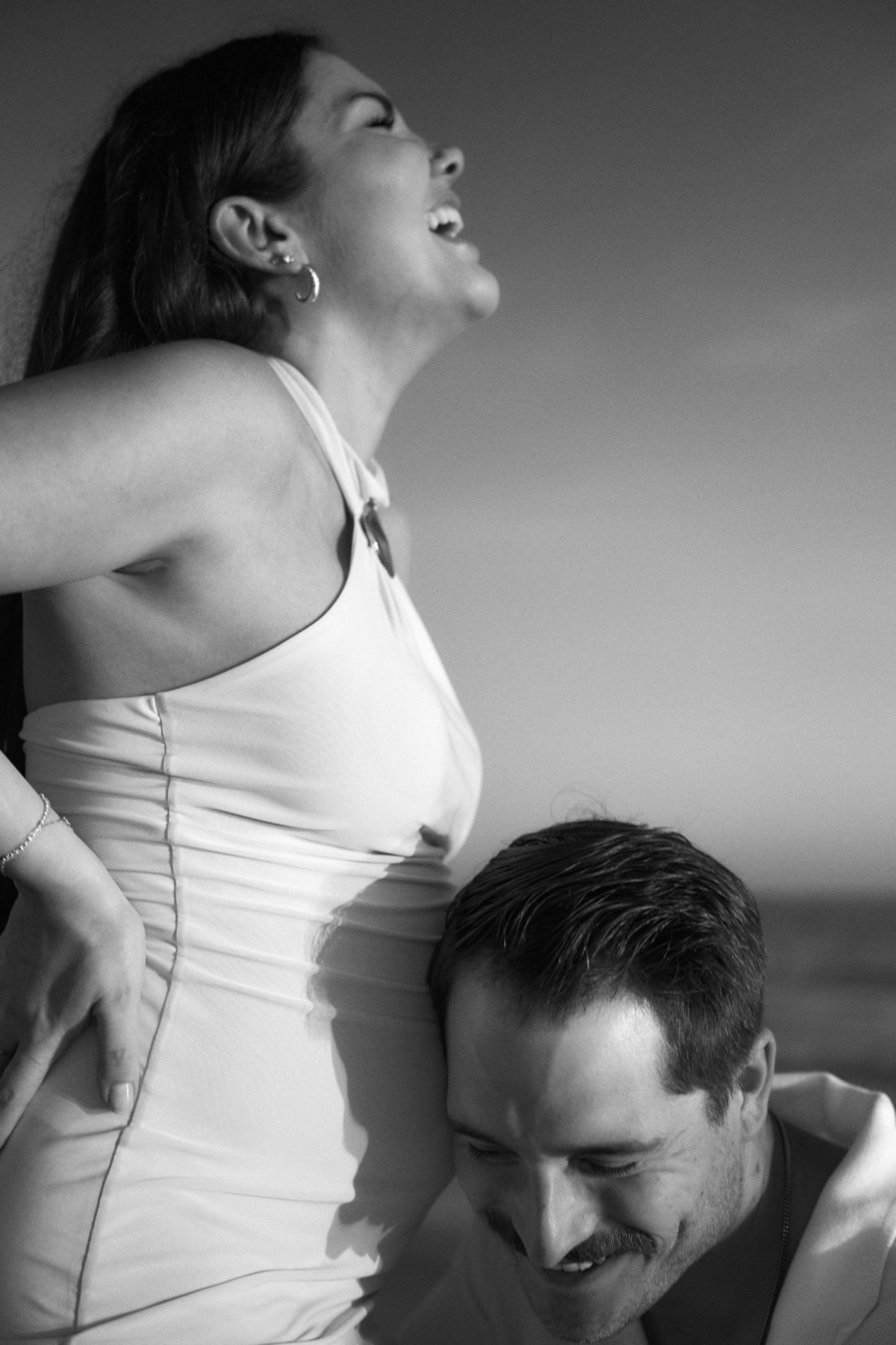 A pregnant woman laughing with her partner on the beach, black and white