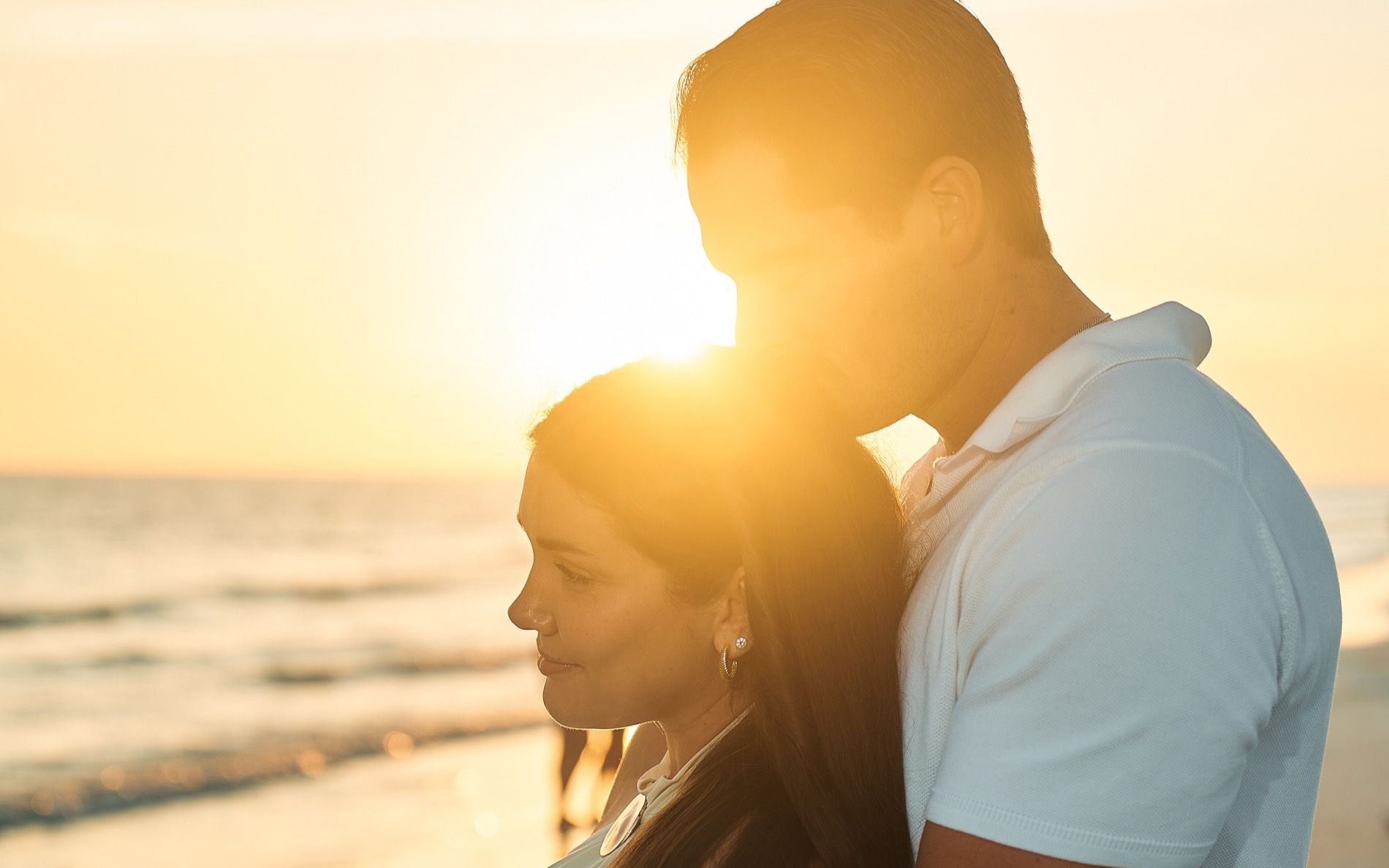 A couple on a Sarasota beach at sunset, the sun behind them over the Gulf