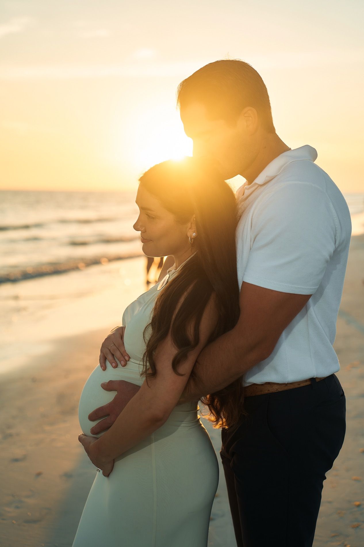 A maternity portrait about half an hour before sunset, the sun low over the Gulf behind the couple