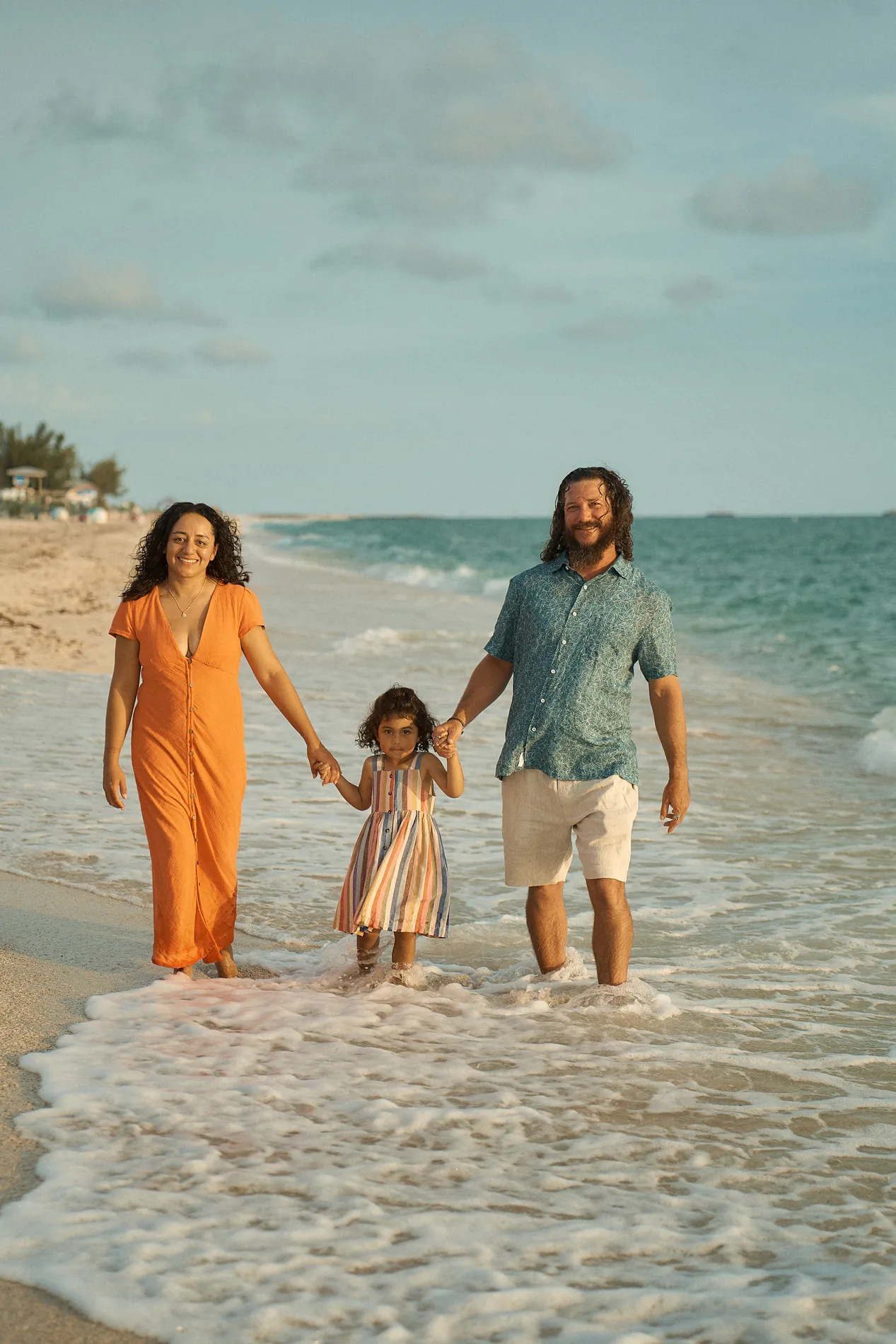Parents walking their small daughter by the hands through the sea foam at Nokomis Beach
