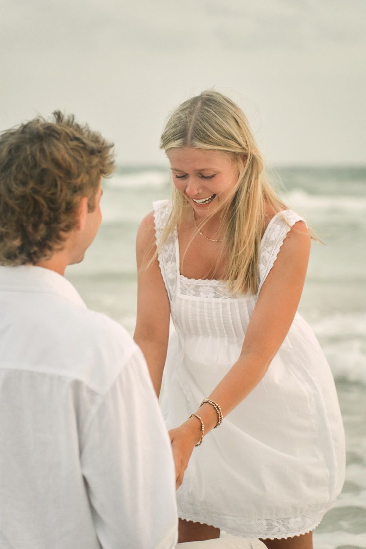 A newly engaged couple laughing right after the proposal on the beach