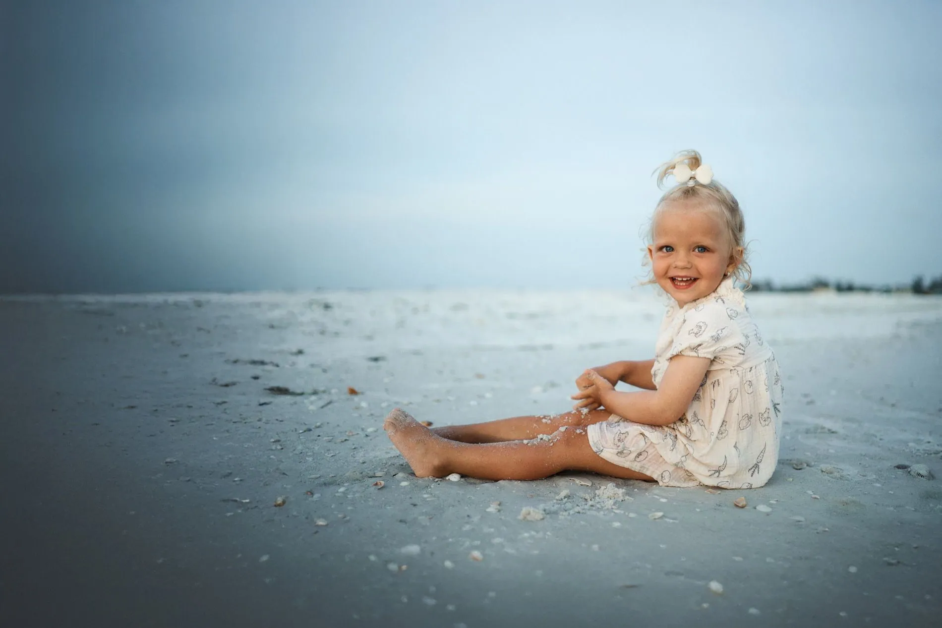 A little girl sitting on the sand among the shells at South Lido Beach in Sarasota