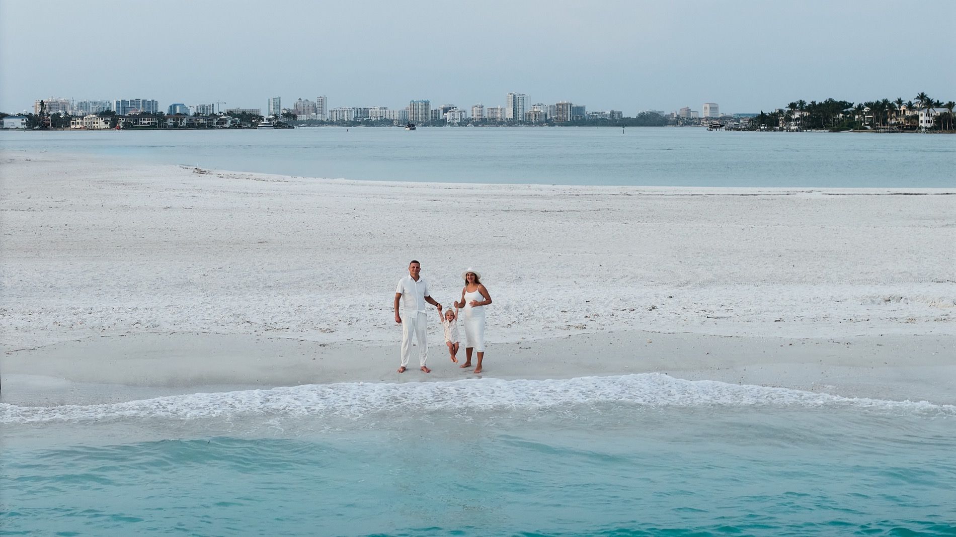 A family on the white sand at South Lido from above, the water on both sides and Sarasota across the bay