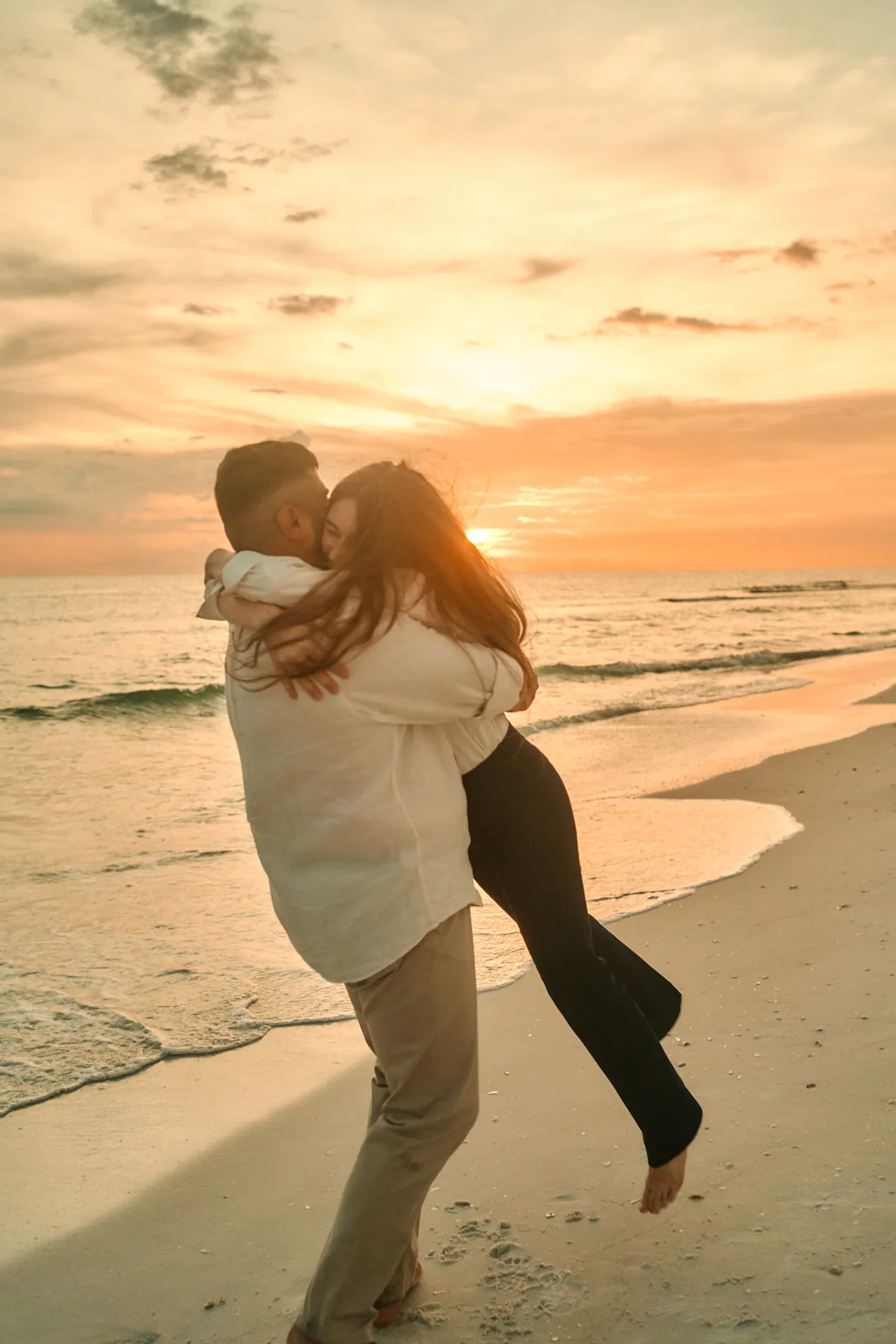 A man spinning a woman in his arms on the sand at sunset, orange sky behind them