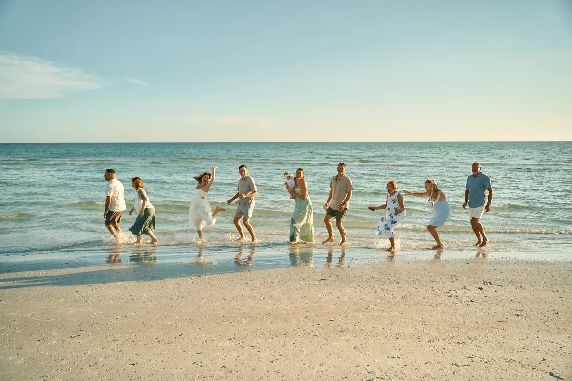 A big family dancing and splashing in a line in the shallow water, seen from across the sand