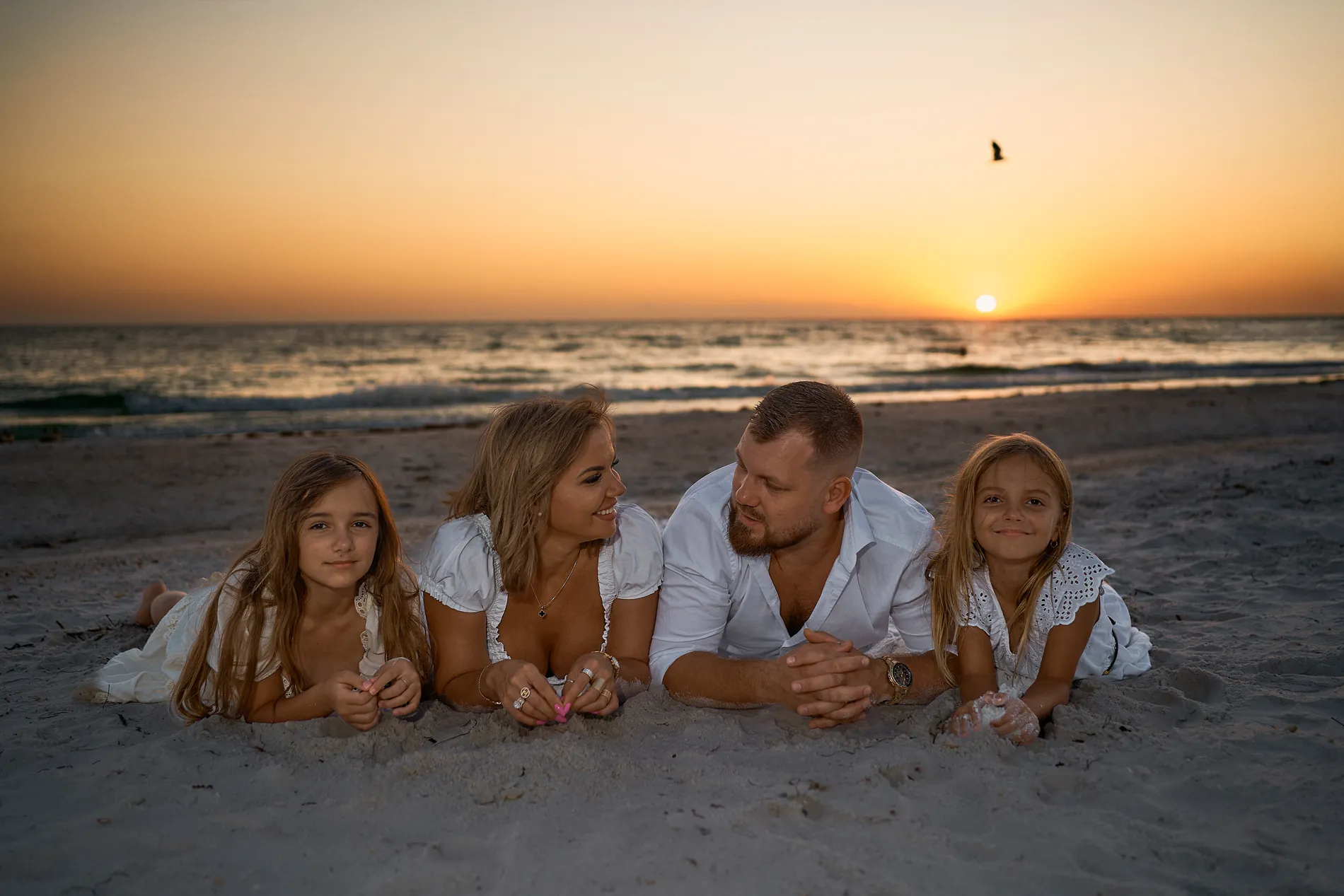Parents and their two daughters lying on the sand on Lido Key and laughing, the sun going down over the Gulf behind them