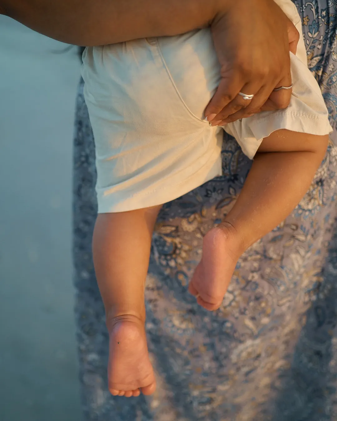 A baby's bare feet hanging over a mother's arm, her hand with a ring holding him, on Siesta Key