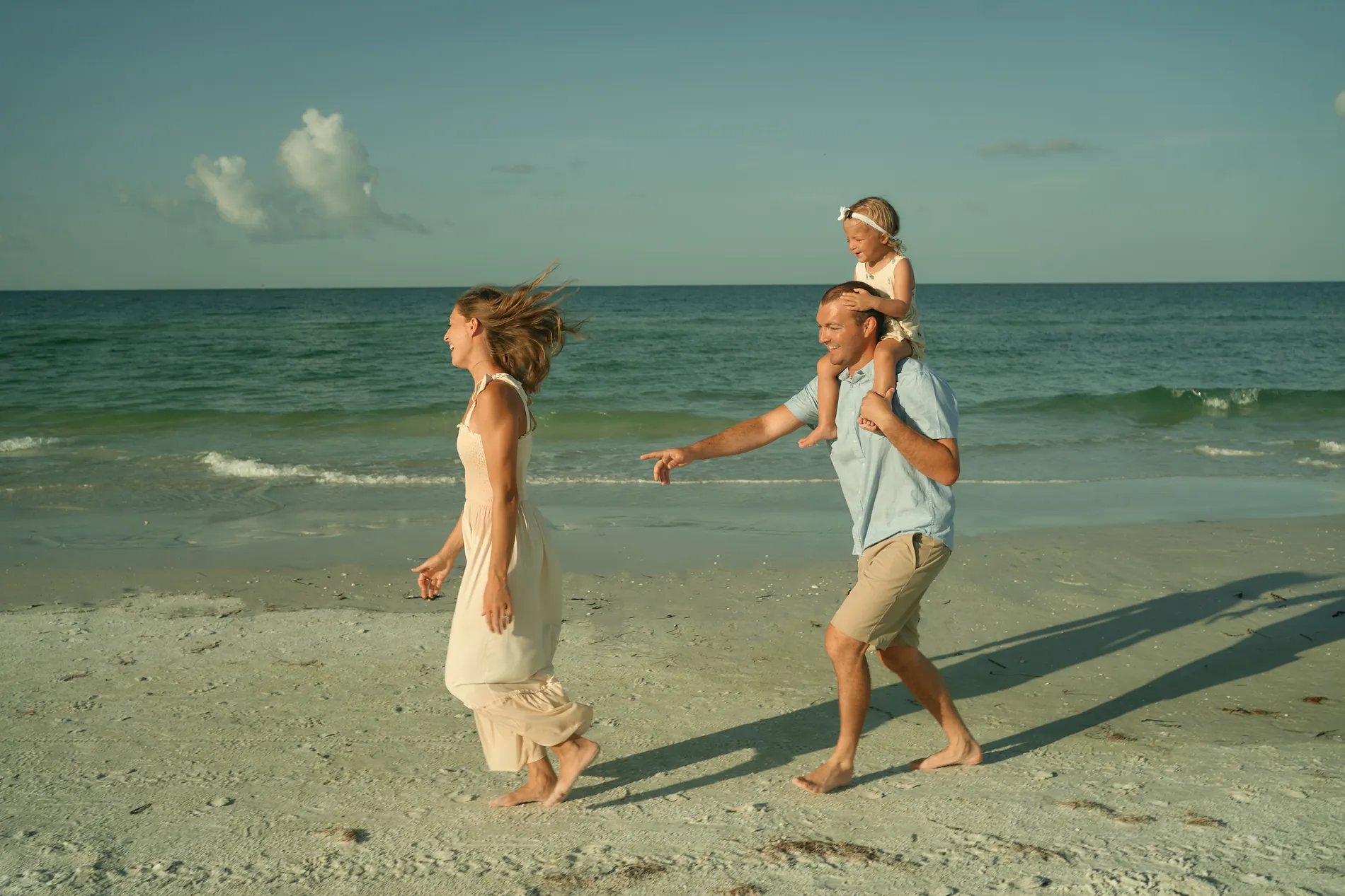 A father carrying his little daughter on his shoulders while the mother spins on the sand beside them on Siesta Key