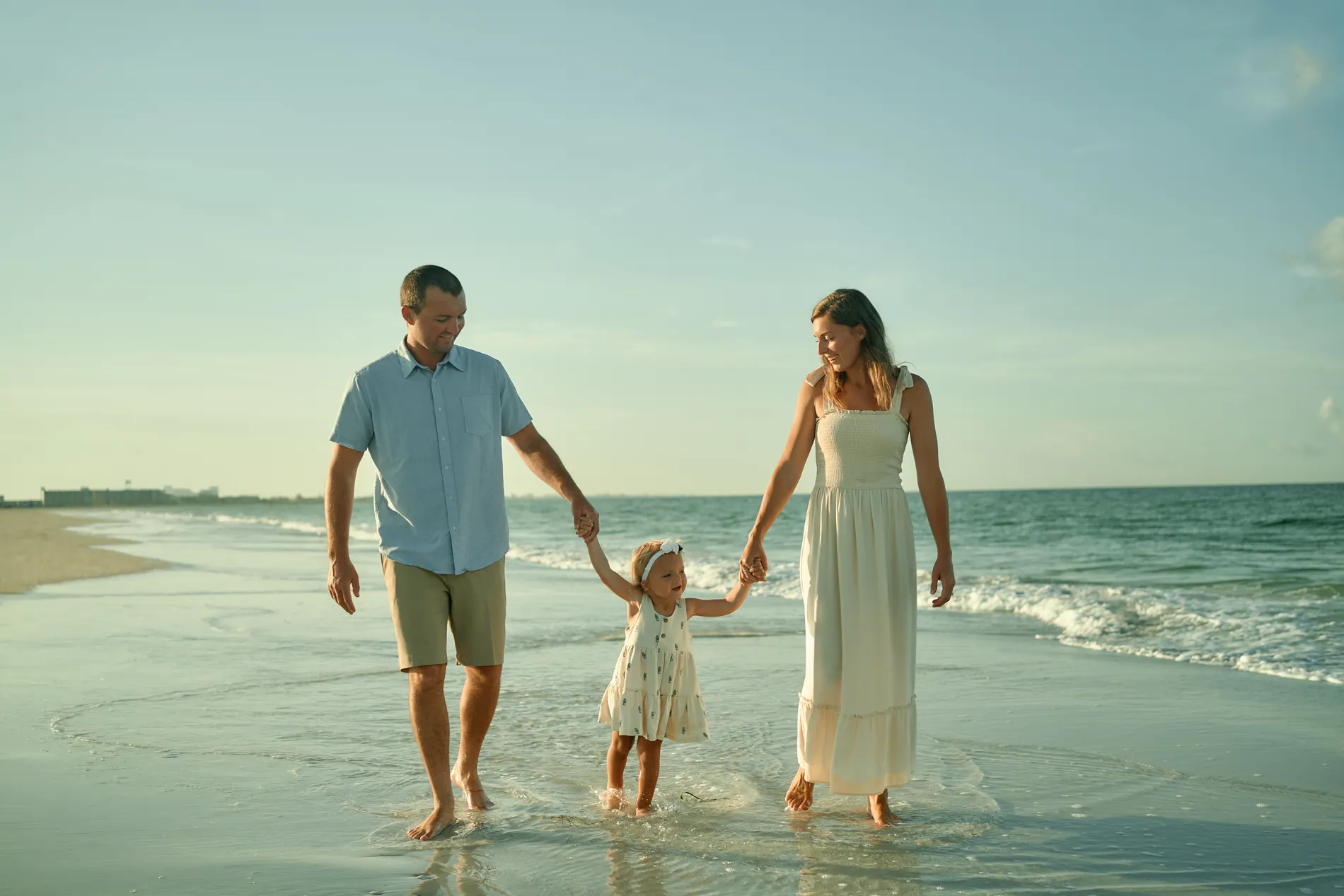 Parents walking their little daughter by the hands through the edge of the surf on Siesta Key