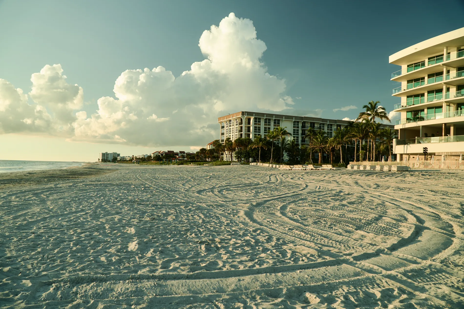 The wide, raked sand in front of The St. Regis Longboat Key in late light, the resort buildings and palms behind and tall clouds over the Gulf