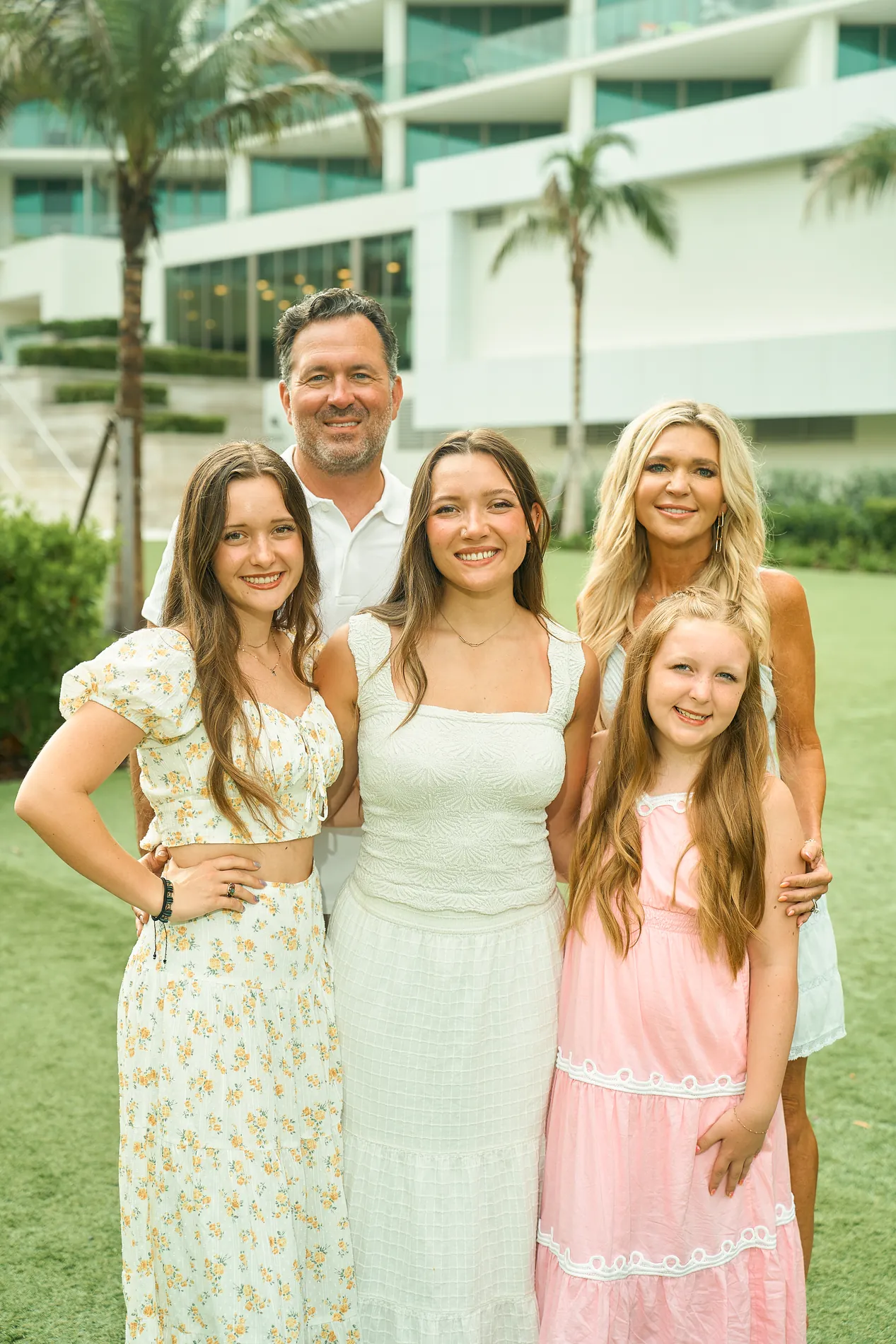 A family of five standing close together on the lawn of The St. Regis Longboat Key, the white hotel tower and palms behind them