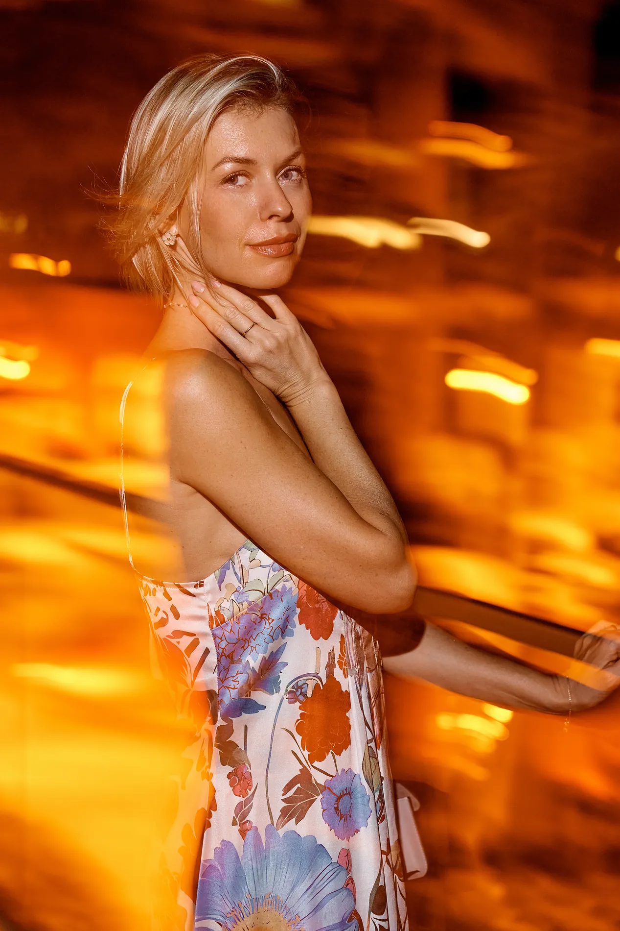Close portrait of a young woman with her hand at her neck, warm streaks of resort lights behind her at night