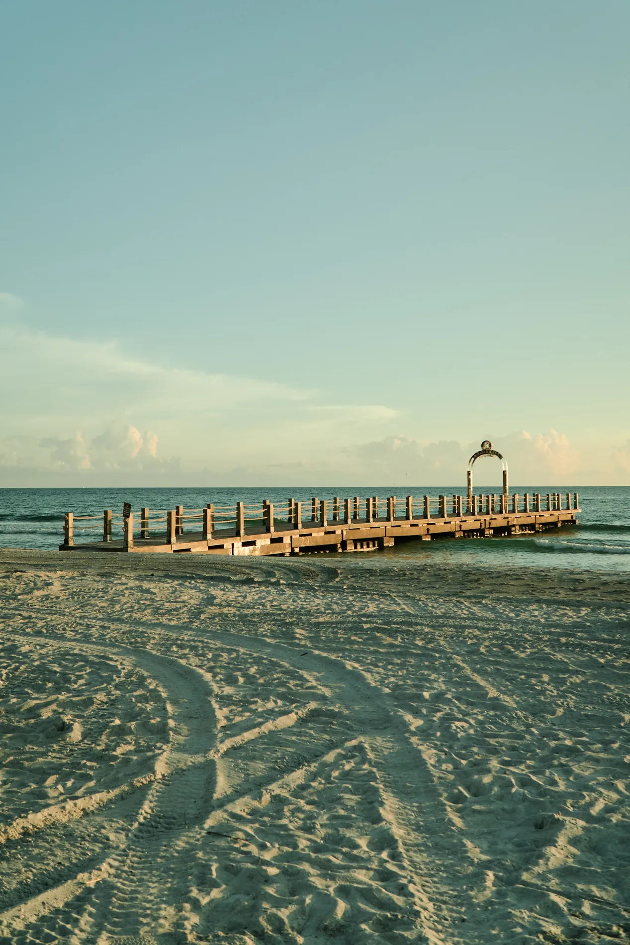 The pier at The St. Regis Longboat Key with its white arch, seen from the raked sand in the evening