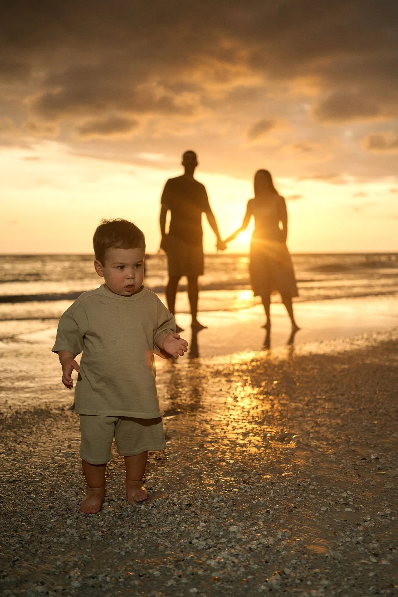 A toddler walking ahead of his parents at sunset